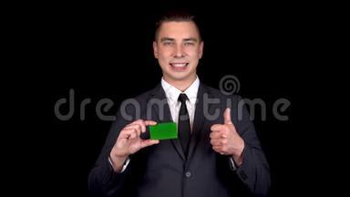 年轻的商人出示了一张银行绿卡，并用他的手表现得像。 彩色绿卡。 穿着黑色西装的男人